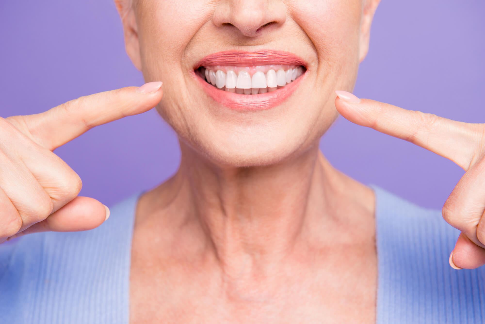 Closeup of woman smiling and pointing at her new dental Implants 29678
